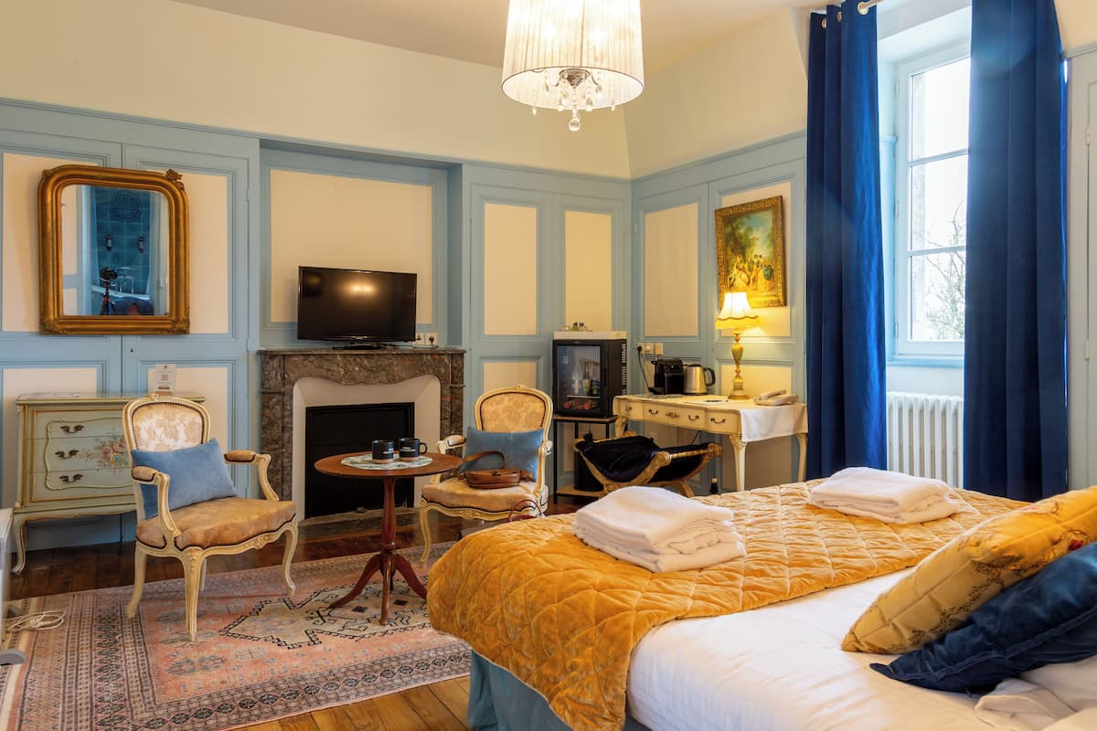 Ein Hotelzimmer mit Bett, Fernseher, Kamin, Schreibtisch mit Lampe und einem Fenster mit Vorhängen.