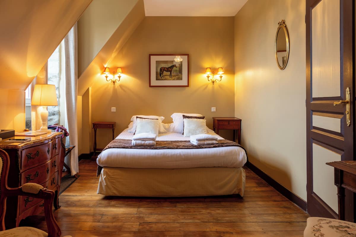 Ein Hotelzimmer mit einem großen Bett, Holzböden, einem Schminktisch, einem Schreibtisch mit Lampe und zwei Wandleuchten.