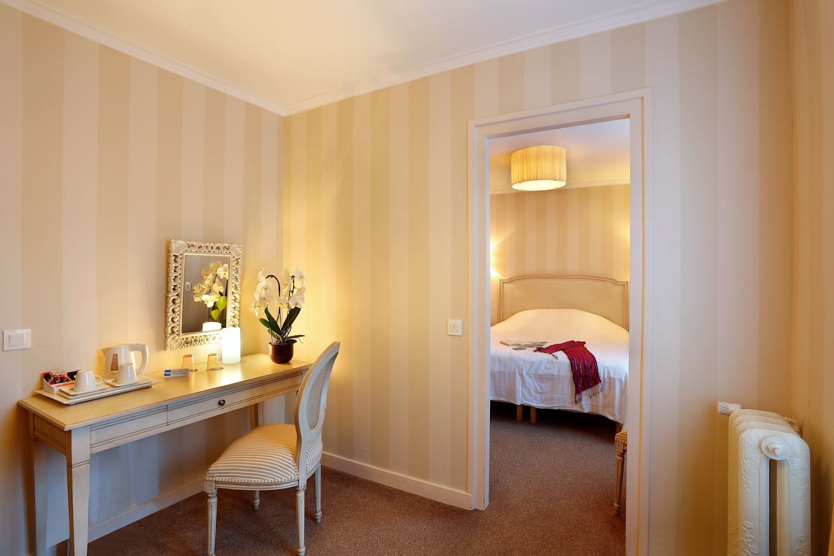Une chambre d’hôtel comprenant un lit, un bureau avec une chaise, un miroir et une table de chevet avec une lampe.