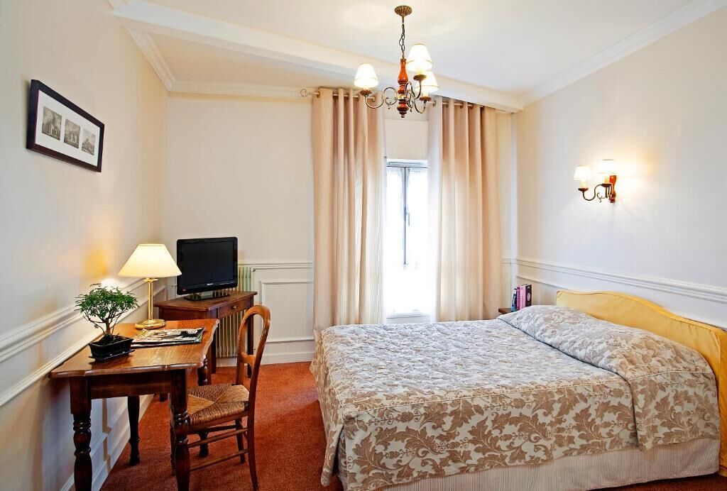 Une chambre d’hôtel avec un lit, un bureau avec une télévision, une chaise, une lampe et un tableau au mur.