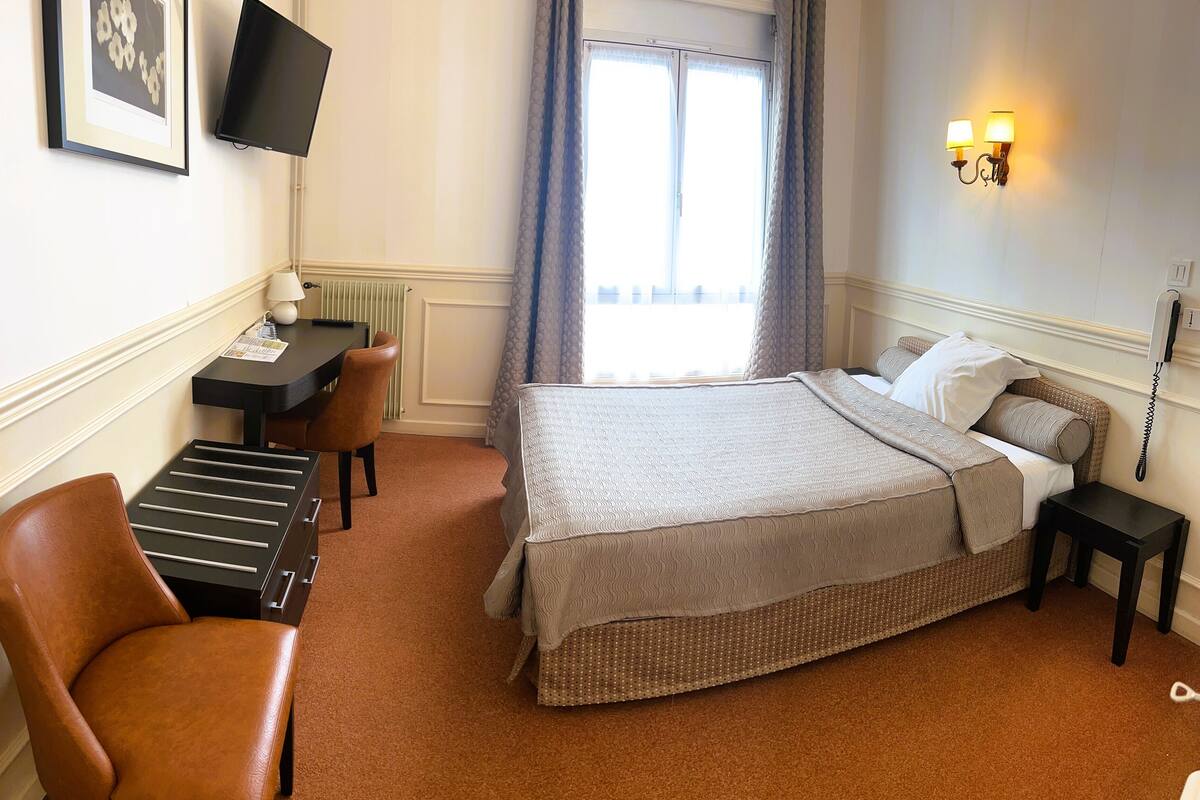Une chambre d’hôtel équipée d’un lit, d’un bureau avec une chaise, d’une télévision et d’un téléphone.
