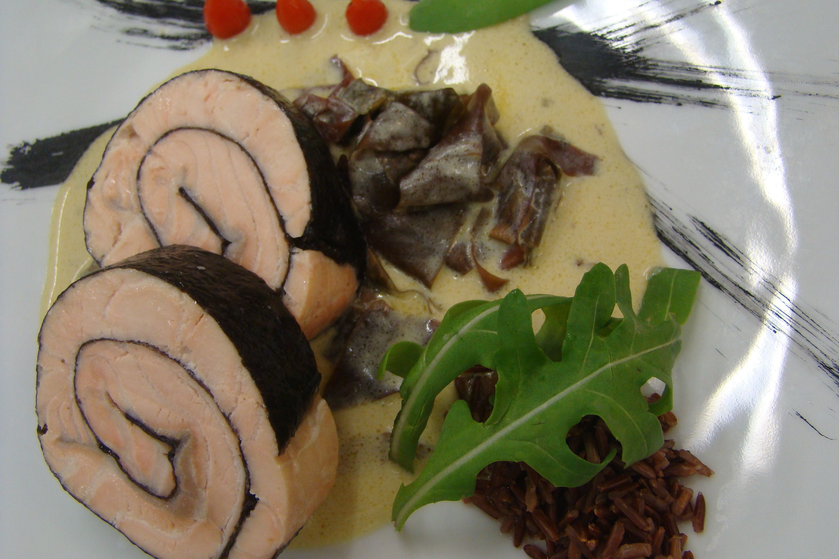 Un plato con carne enrollada, vegetales verdes y granos.