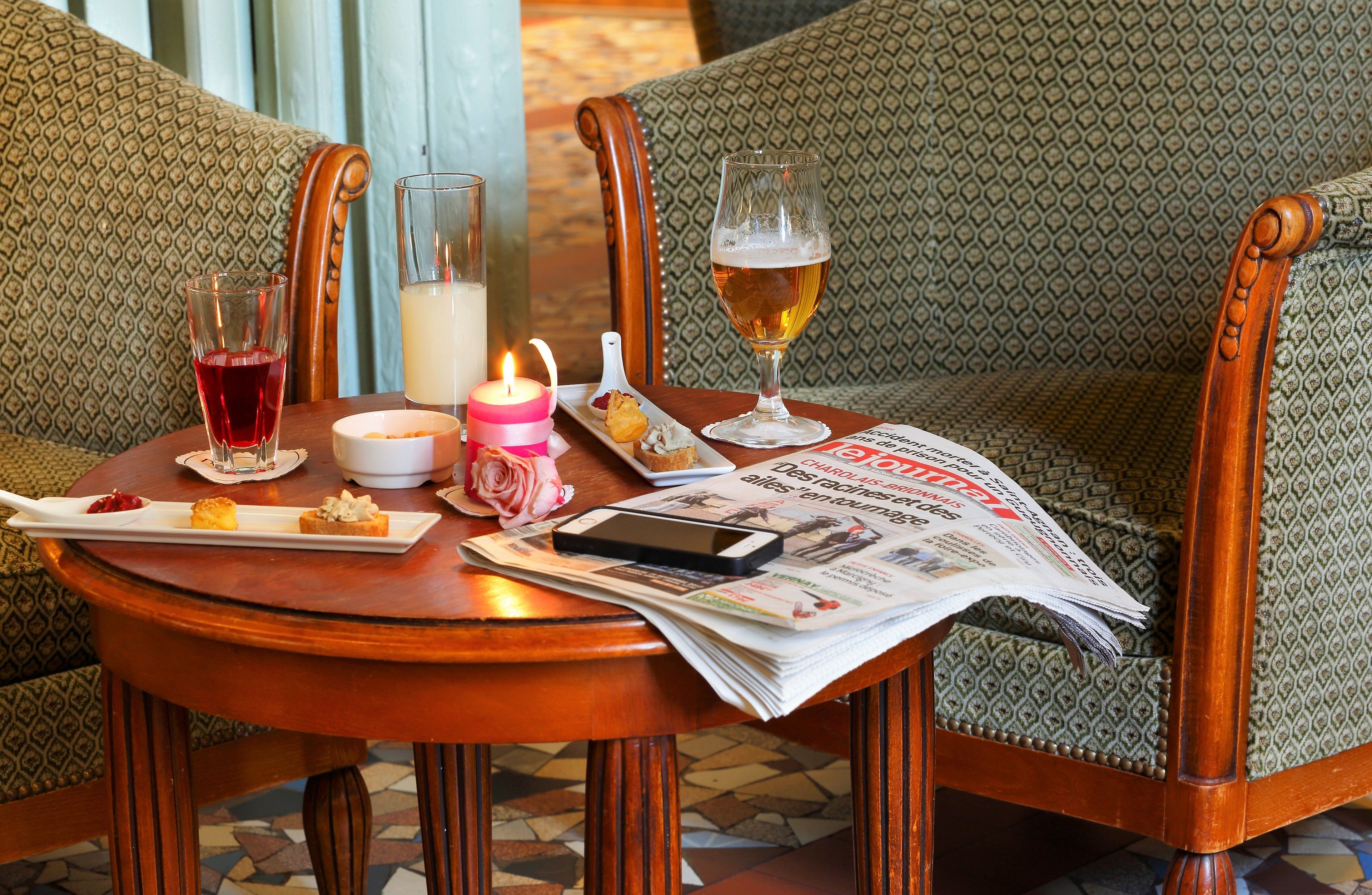Een eettafel met een krant, een biertje, een kaars en een bord eten.