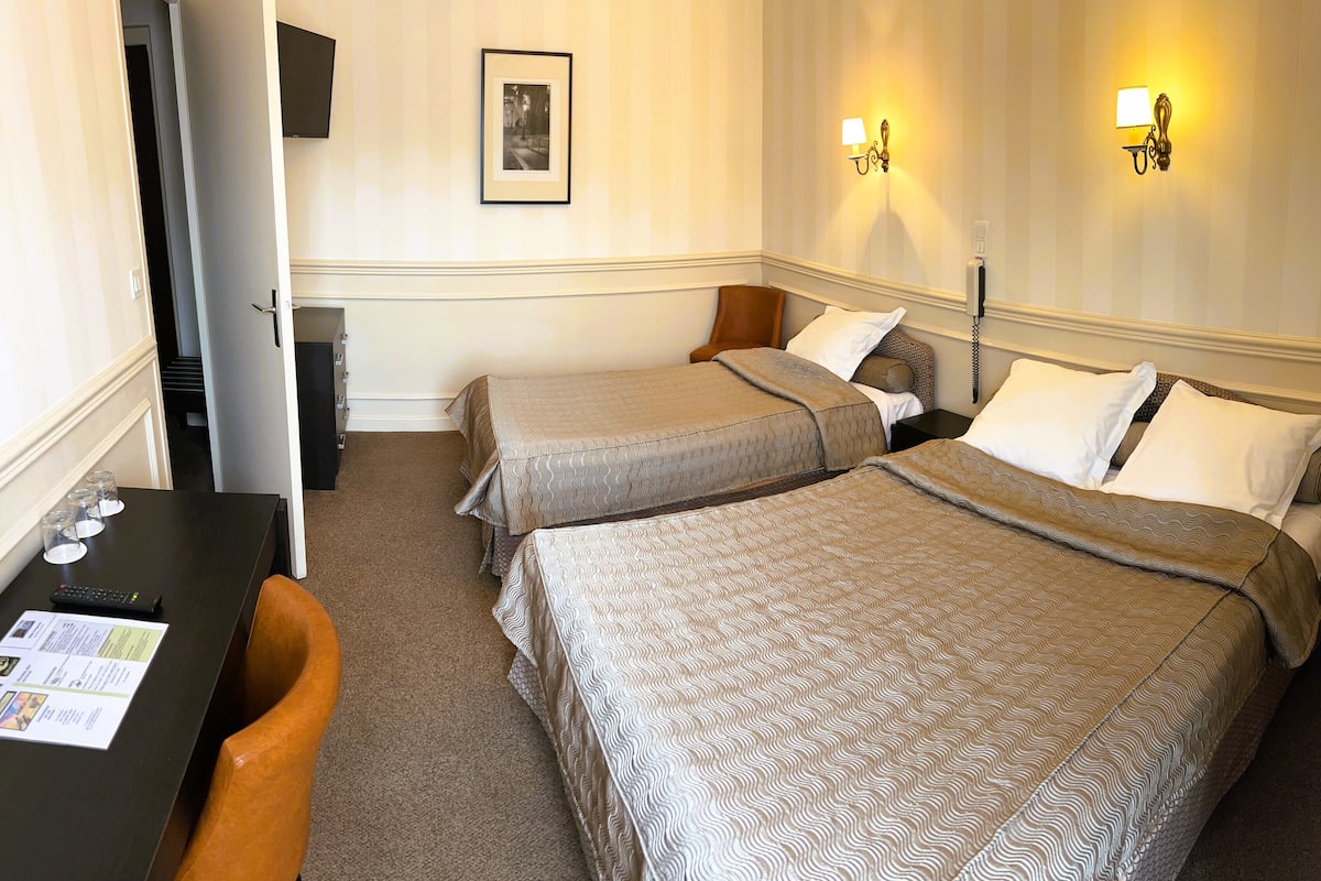 Une chambre d’hôtel avec deux lits, un bureau avec une chaise, un téléphone et un tableau encadré au mur.