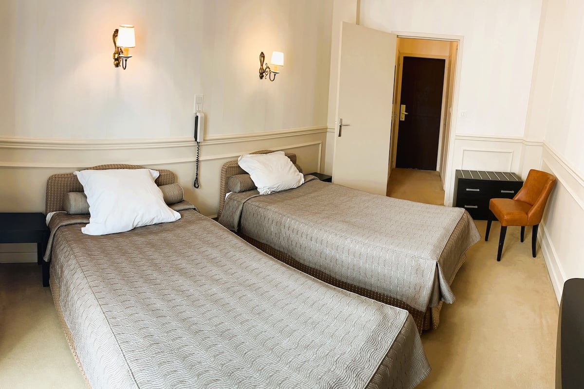 Une chambre d’hôtel avec deux lits simples, un bureau, une chaise et une armoire.