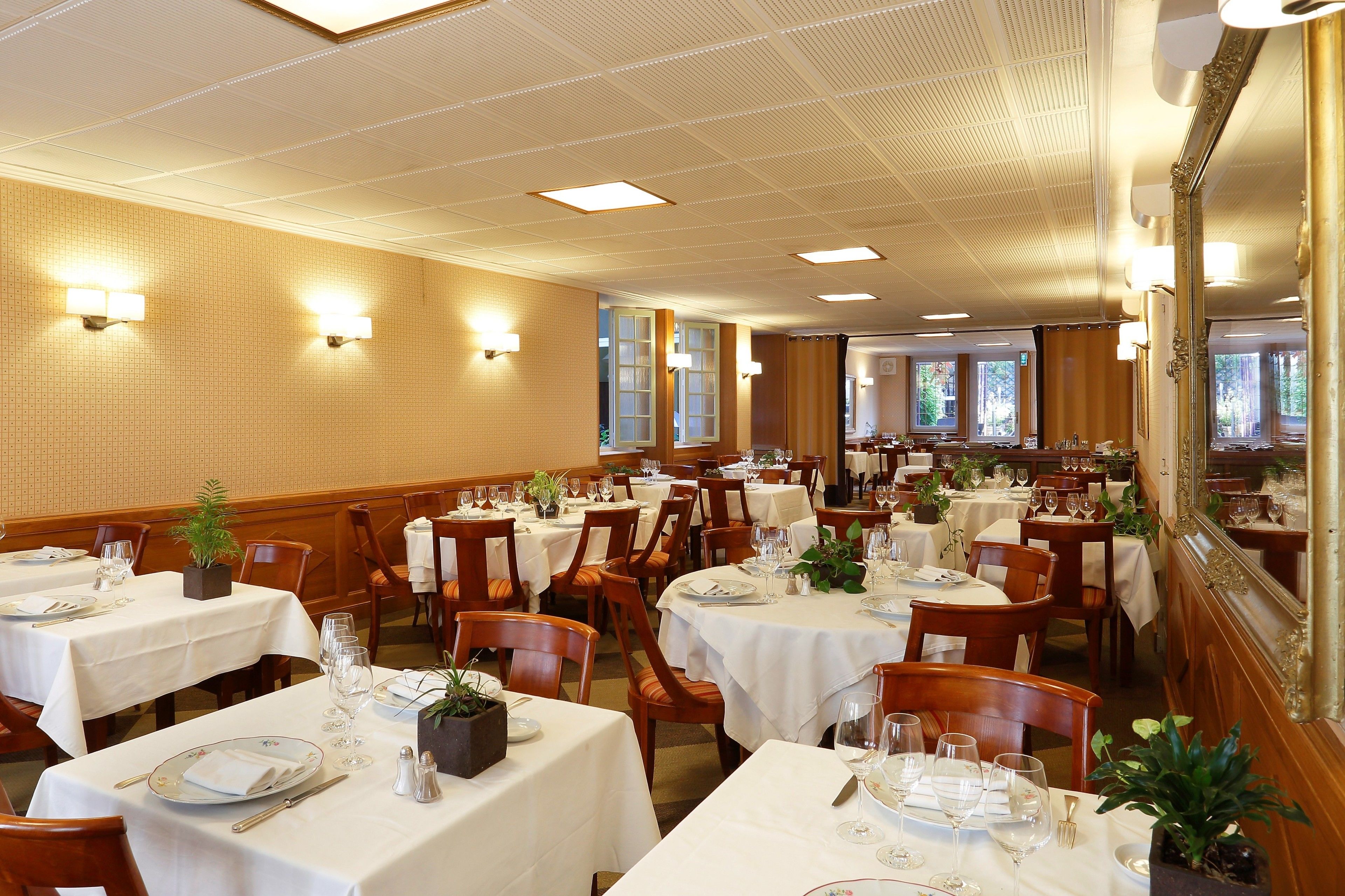A dining area with multiple tables set for service, each with white tablecloths, chairs, and glassware.