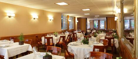 A dining area with multiple tables set for service, each with white tablecloths, chairs, and glassware.