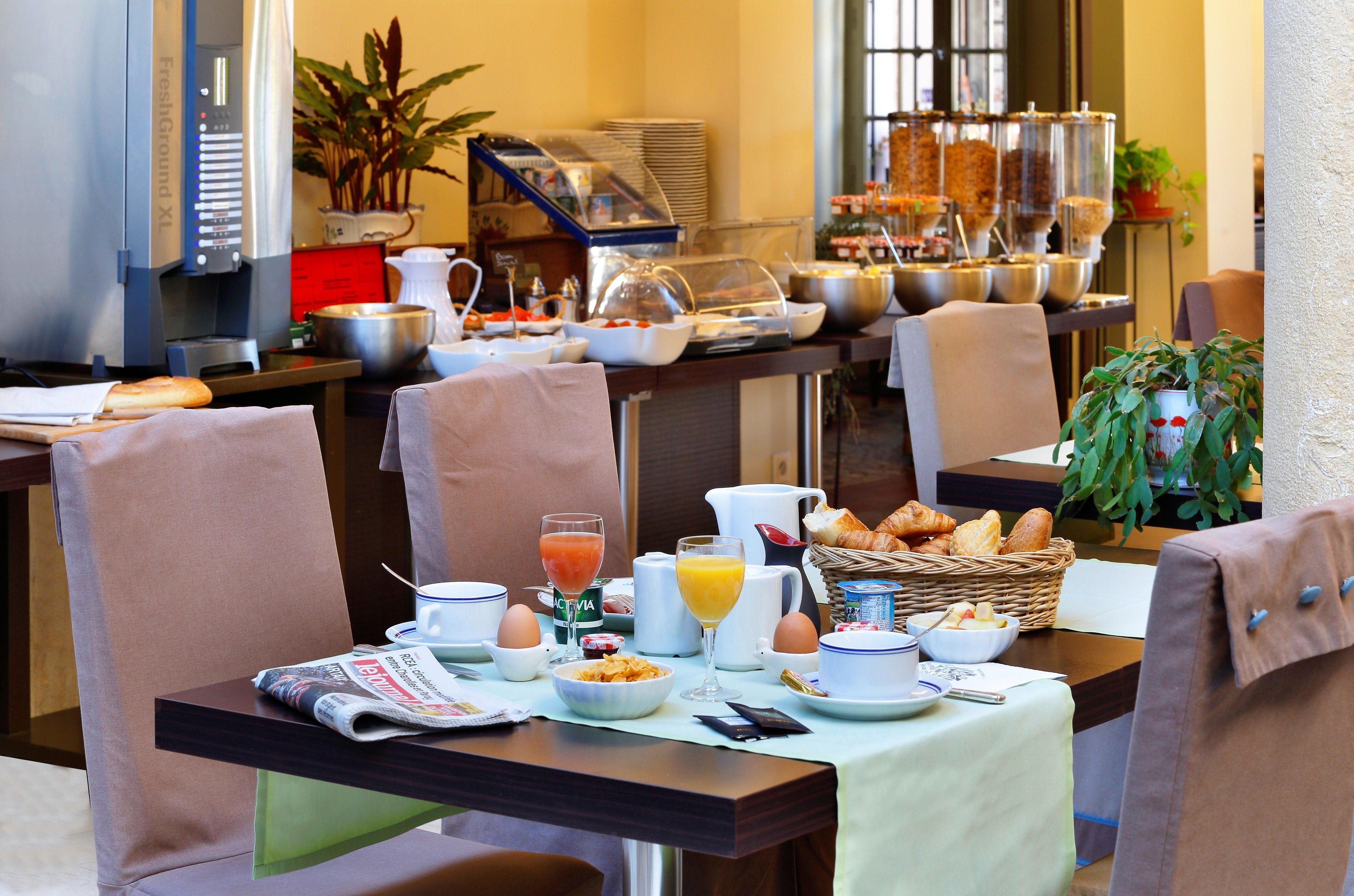 A breakfast buffet setup with various food items, a coffee machine, and seating arrangements.