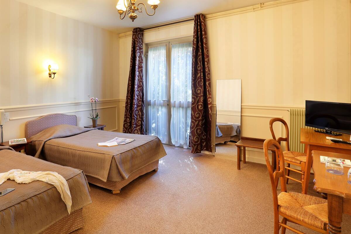 Une chambre d’hôtel avec deux lits, un bureau avec une télévision et un coin repas avec des chaises.