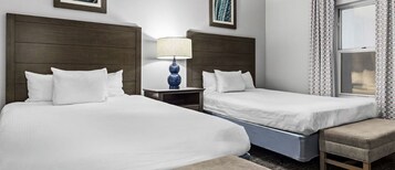 Habitación de hotel con dos camas, una mesita de noche con lámpara, una ventana con cortinas estampadas y un pequeño banco.