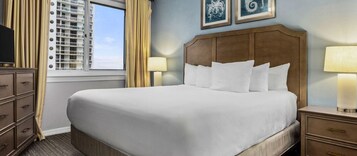 Habitación de hotel con una cama grande, un aparador, una mesita de noche, dos lámparas de pared y una ventana con persianas.