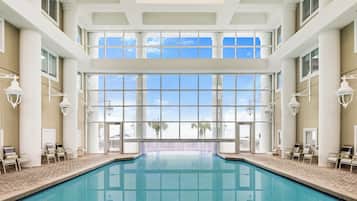 A large indoor swimming pool with clear glass walls, multiple windows, and a tiled floor.