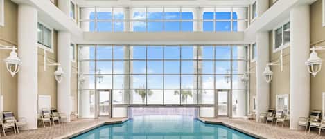 A large indoor swimming pool with clear glass walls, multiple windows, and a tiled floor.