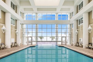Una gran piscina interior con paredes de vidrio transparente, múltiples ventanas y piso de baldosas.