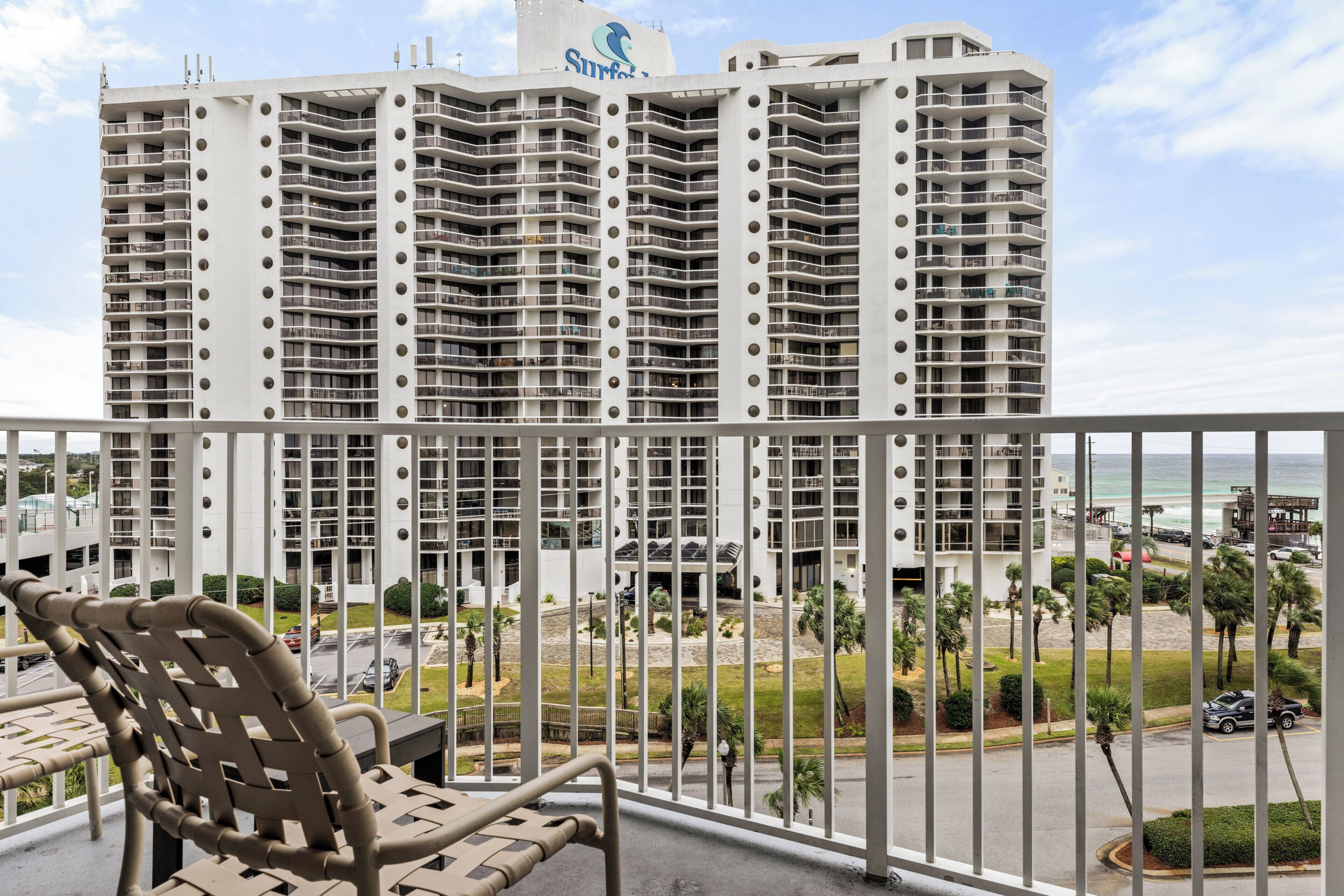 Un hotel de gran altura con varios balcones, vista a la playa y una silla en el balcón.