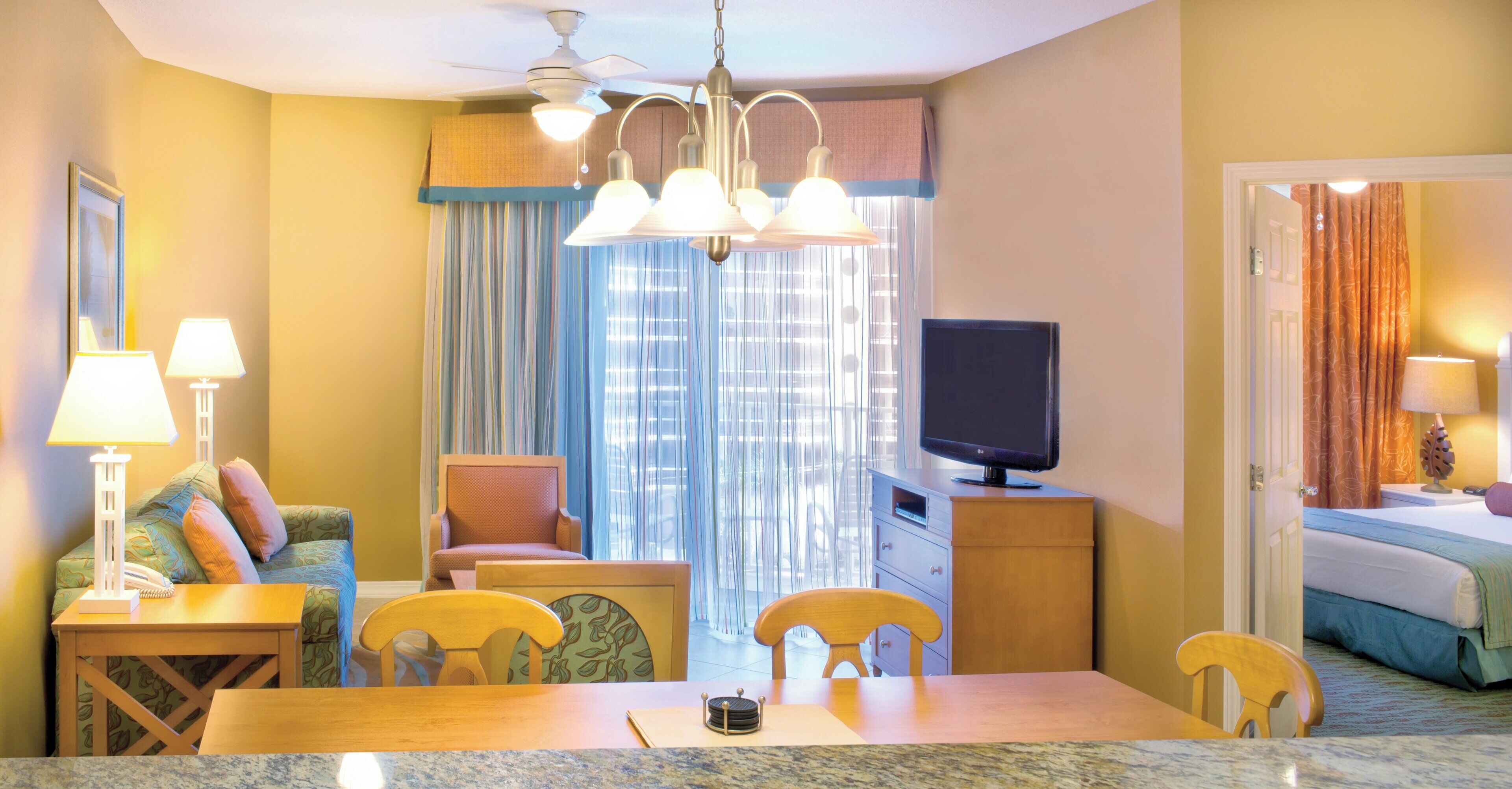 A hotel room with a dining area, a television, a bed, and a window with curtains.