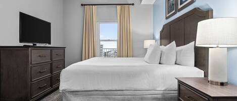 Una habitación de hotel con cama, televisión, cómoda y ventana con cortinas.