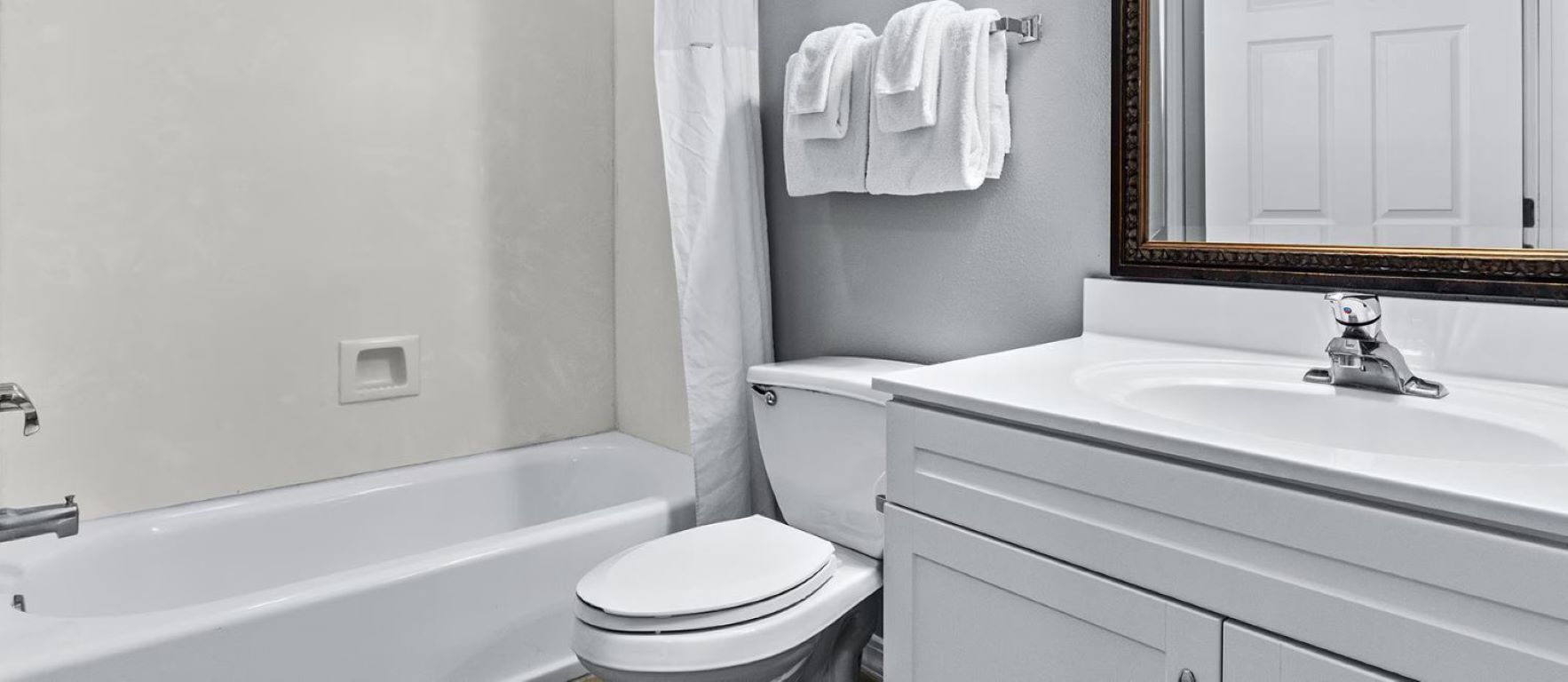 A bathroom with a bathtub, toilet, sink, and a mirror with a decorative frame.