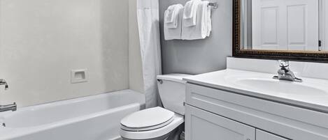 A bathroom with a bathtub, toilet, sink, and a mirror with a decorative frame.
