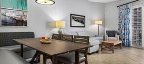 A dining area with a table, chairs, a sofa, and a small side table. There are two lamps, a framed picture on the wall, and a patterned curtain. - Club Wyndham at Majestic Sun (Miramar Beach)