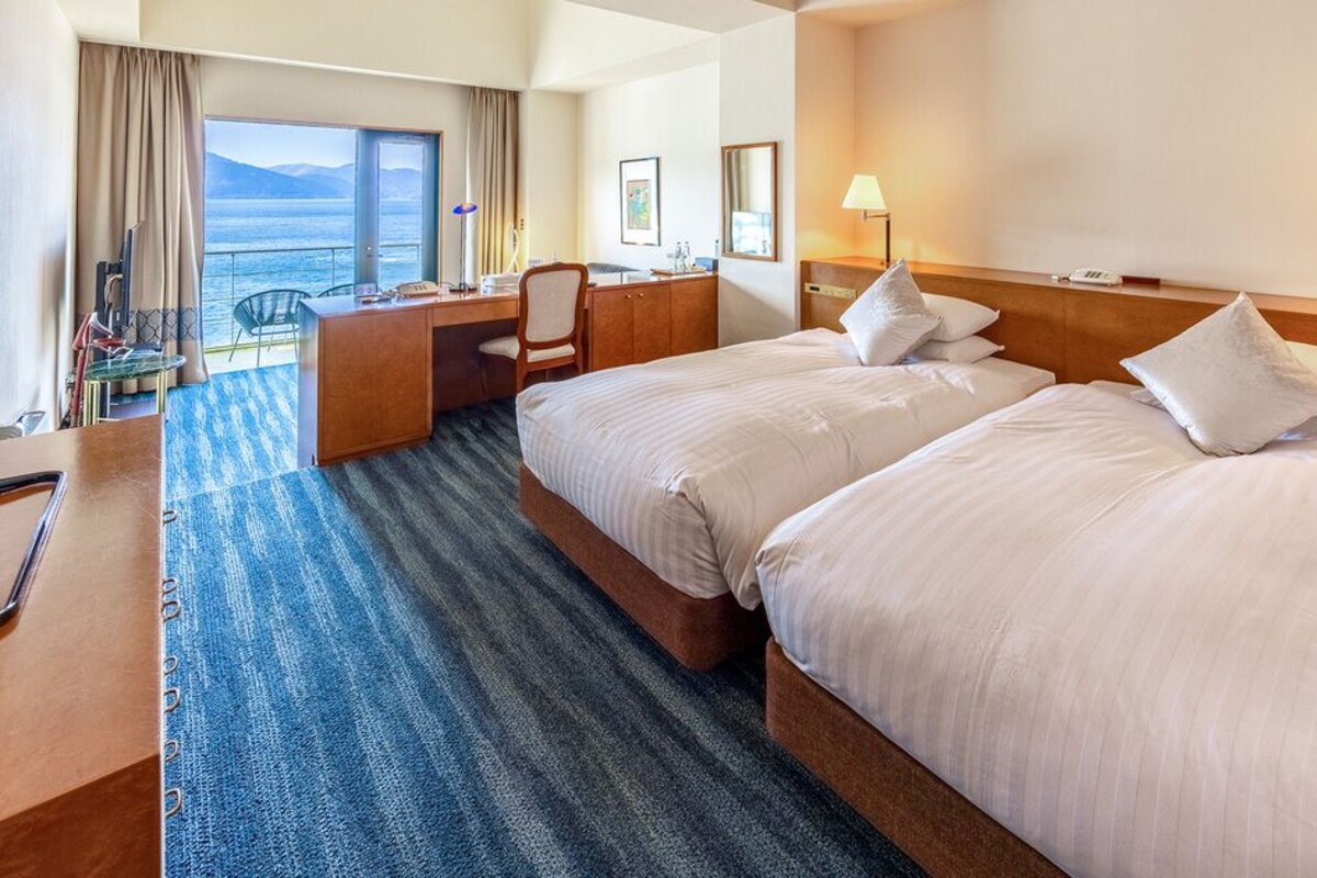 Habitación de hotel con dos camas, un escritorio, una silla, una lámpara de escritorio y vistas al mar.