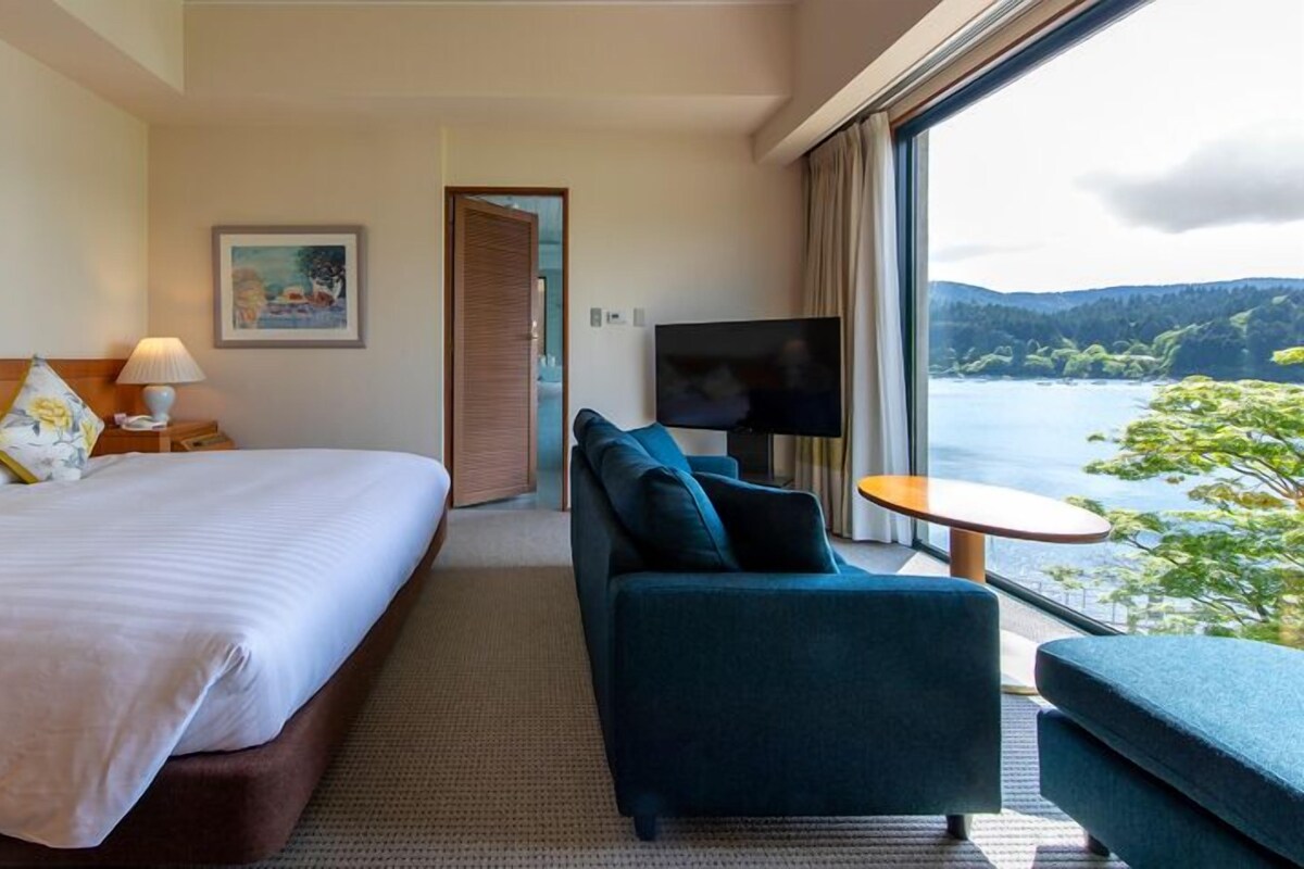 Una habitación de hotel con cama, sofá, televisor y vista al lago.