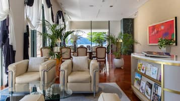 Eine moderne Lobby mit einem Glastisch, beigen Sofas, einem Empfangsbereich mit Bücherpräsentation und Blumentöpfen.