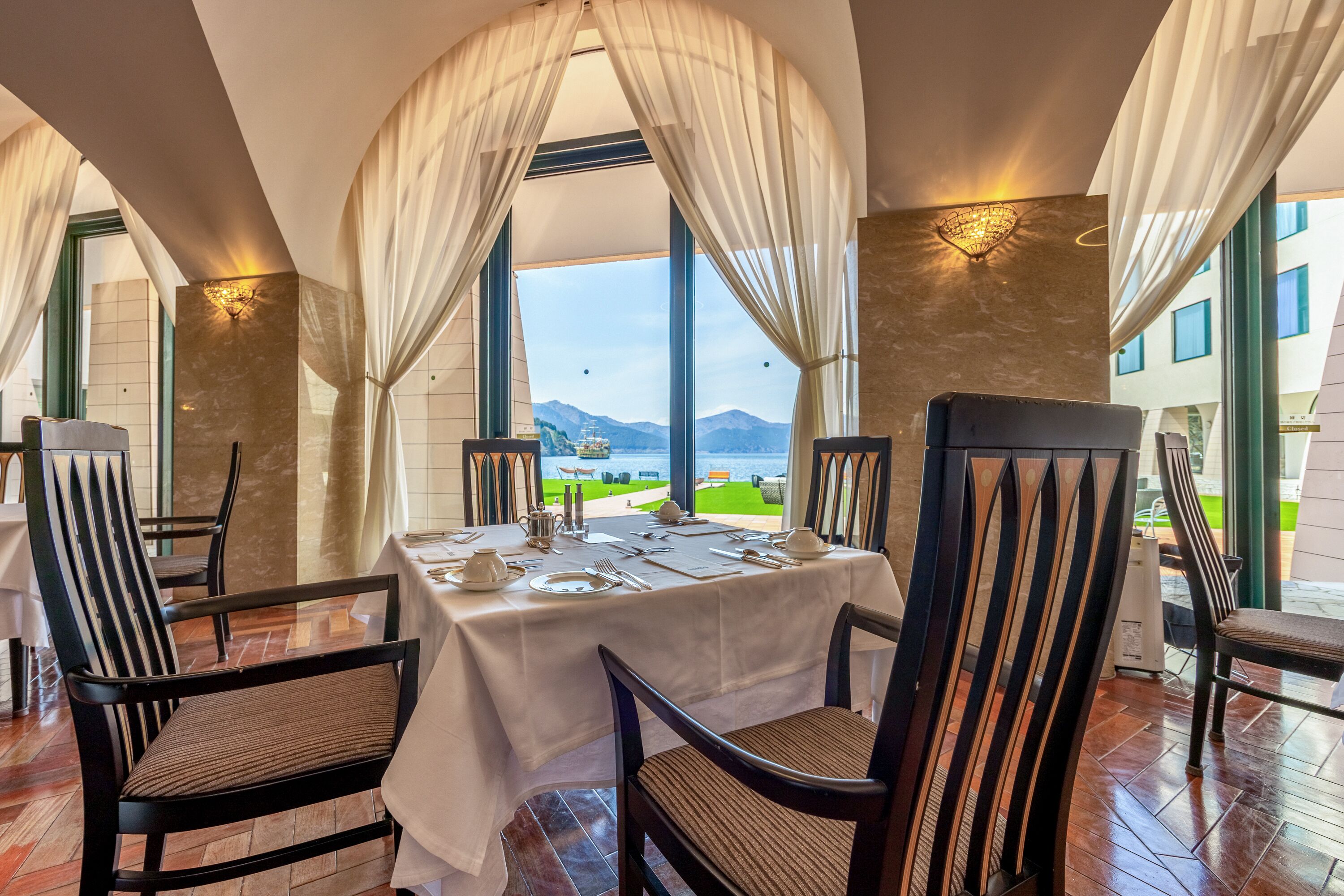 Un coin repas avec une table dressée pour quatre personnes, des chaises et une vue sur les montagnes grâce à de grandes fenêtres.