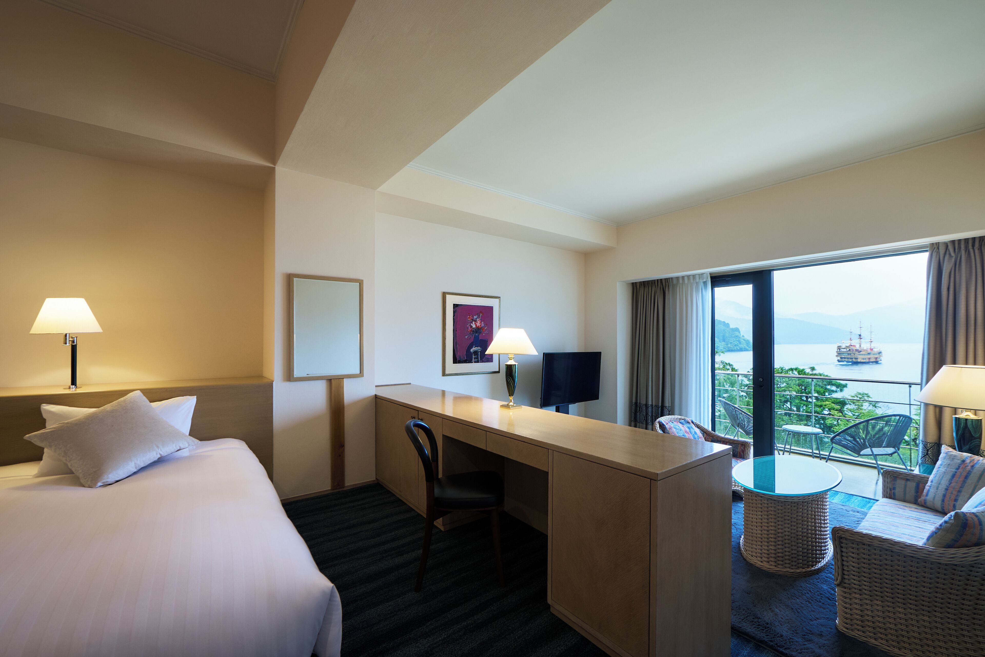 Ein Hotelzimmer mit Bett, Schreibtisch, Stuhl und einem Balkon mit Meerblick.