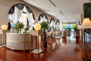 A spacious lobby with a wooden floor, a reception desk, and a seating area with chairs and tables.