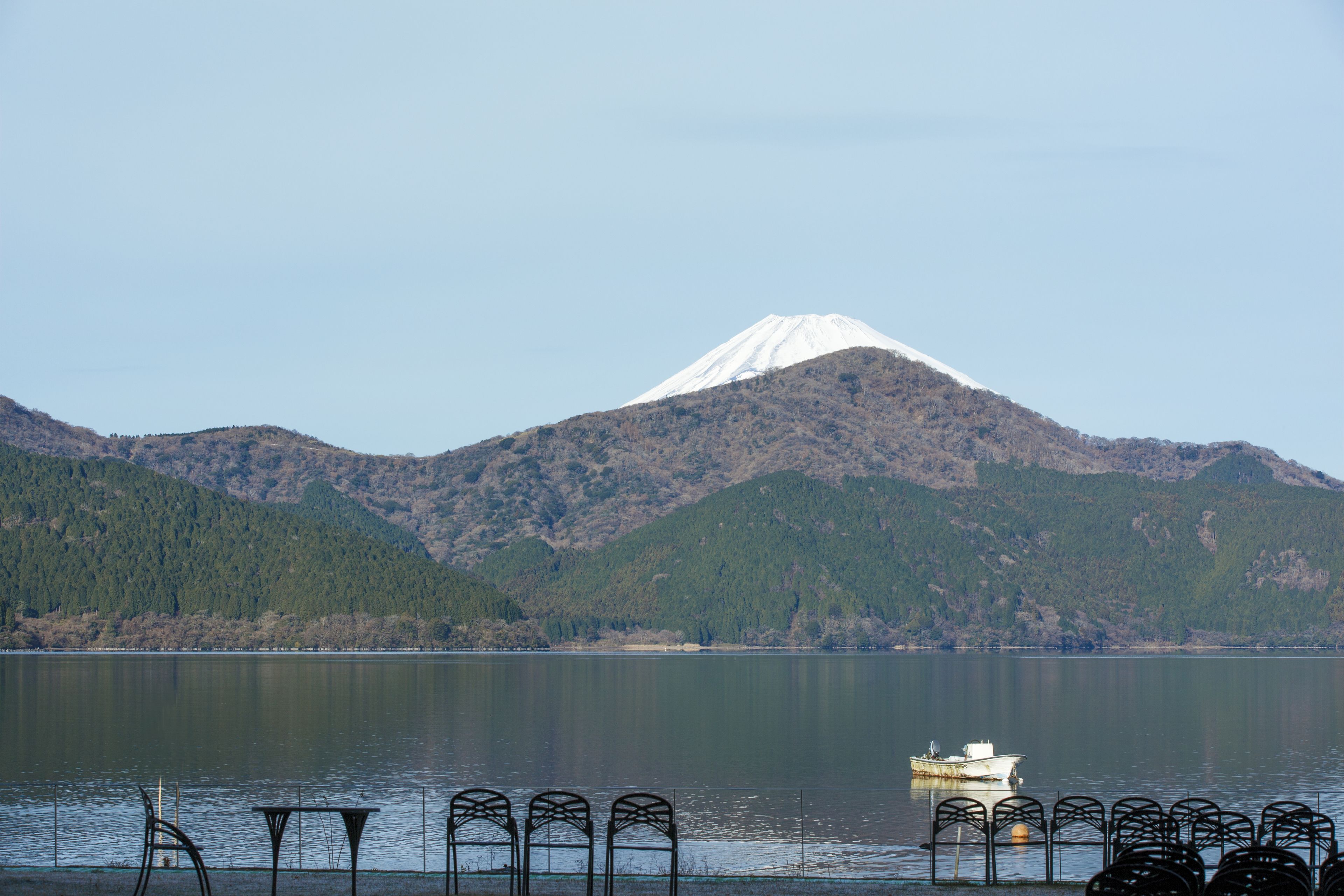 A lake with a boat, metal chairs, and a mountain in the background.