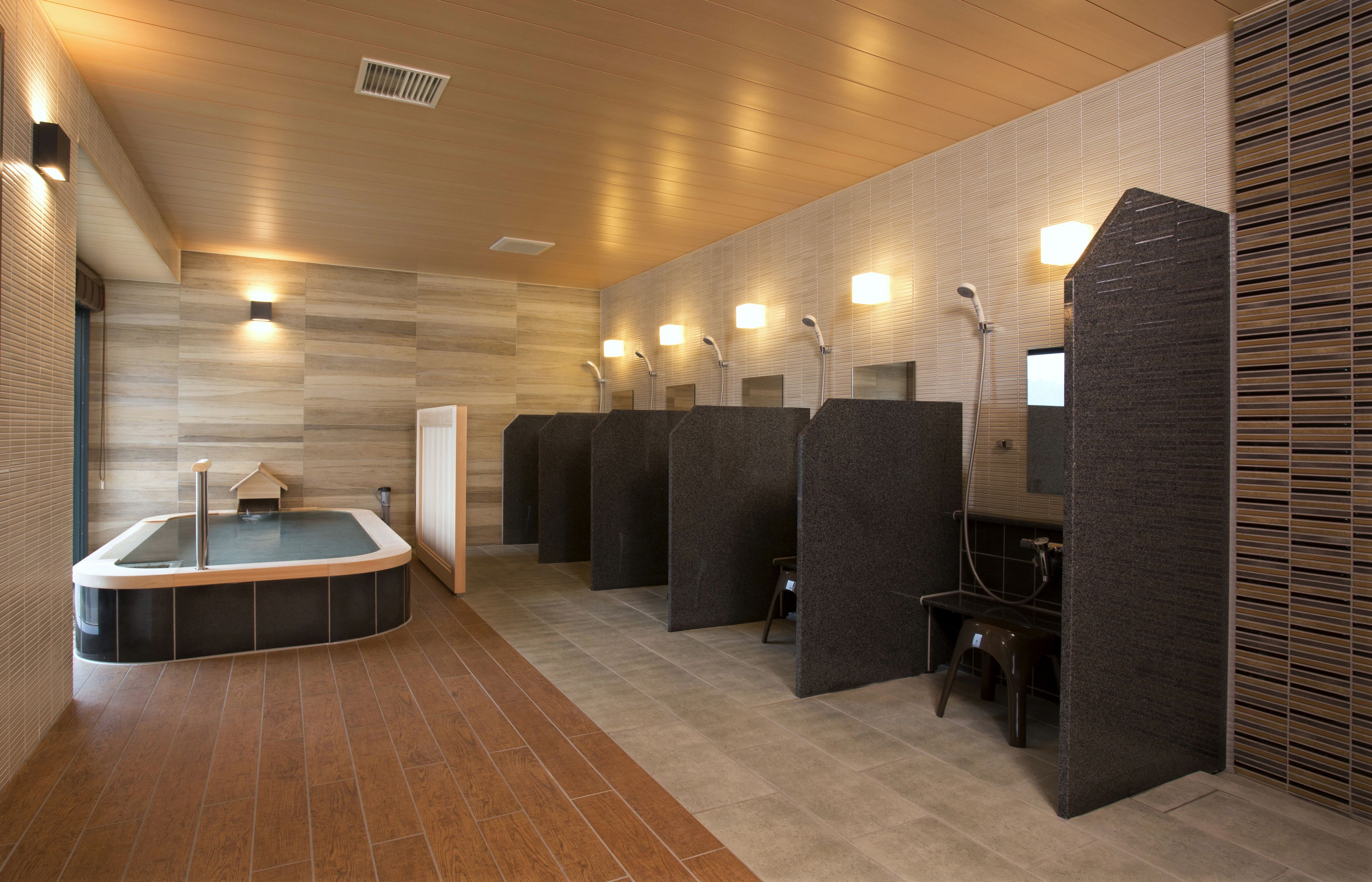 Une salle de bain moderne dotée d’un grand jacuzzi central, de plusieurs cabines de douche et d’un plancher en bois.