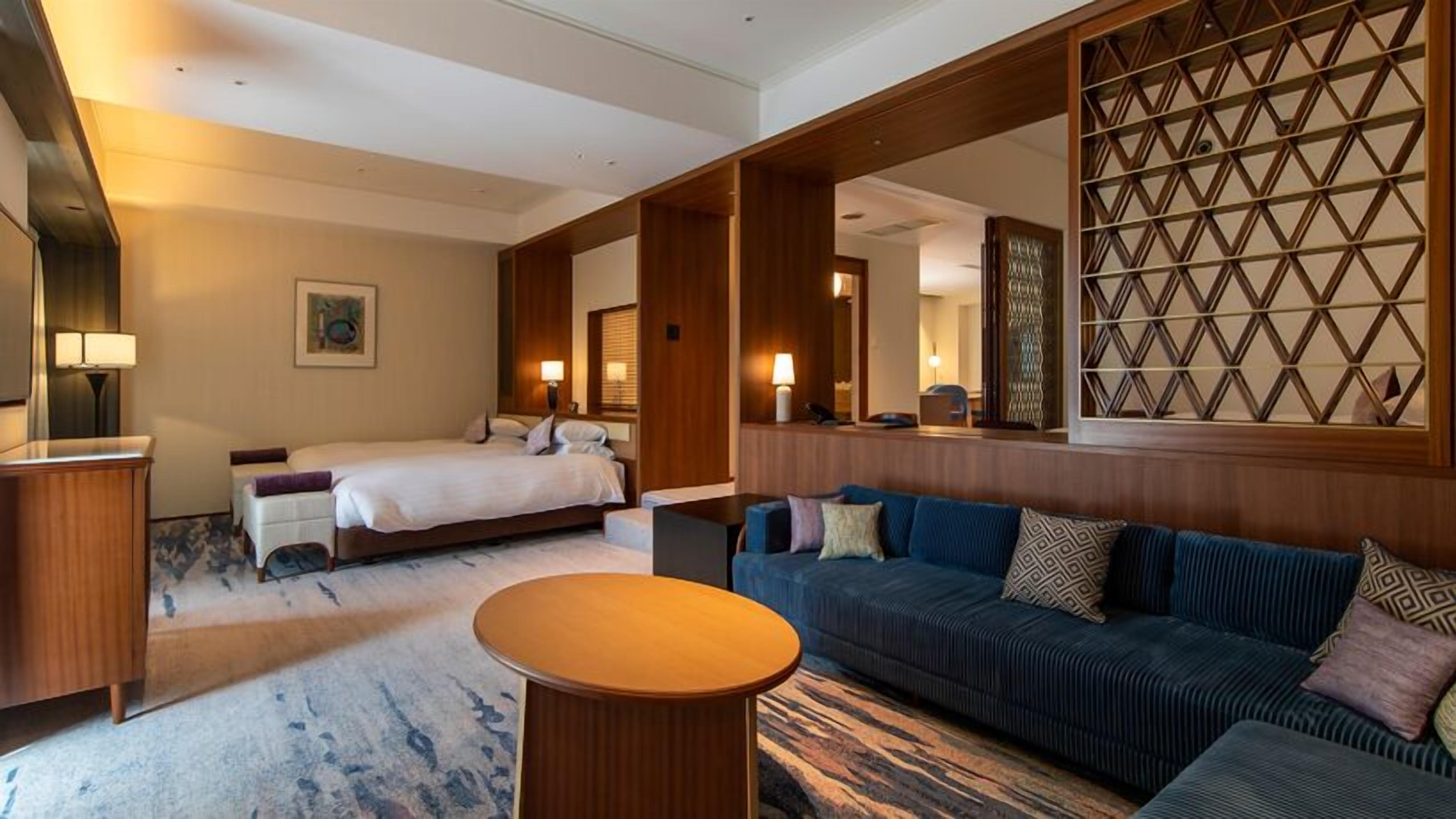 A hotel room with a bed, a sofa, a small table, and a decorative wall panel.