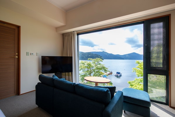 A room with a large window offering a view of a lake and mountains. - Hakone Hotel (Hakone)