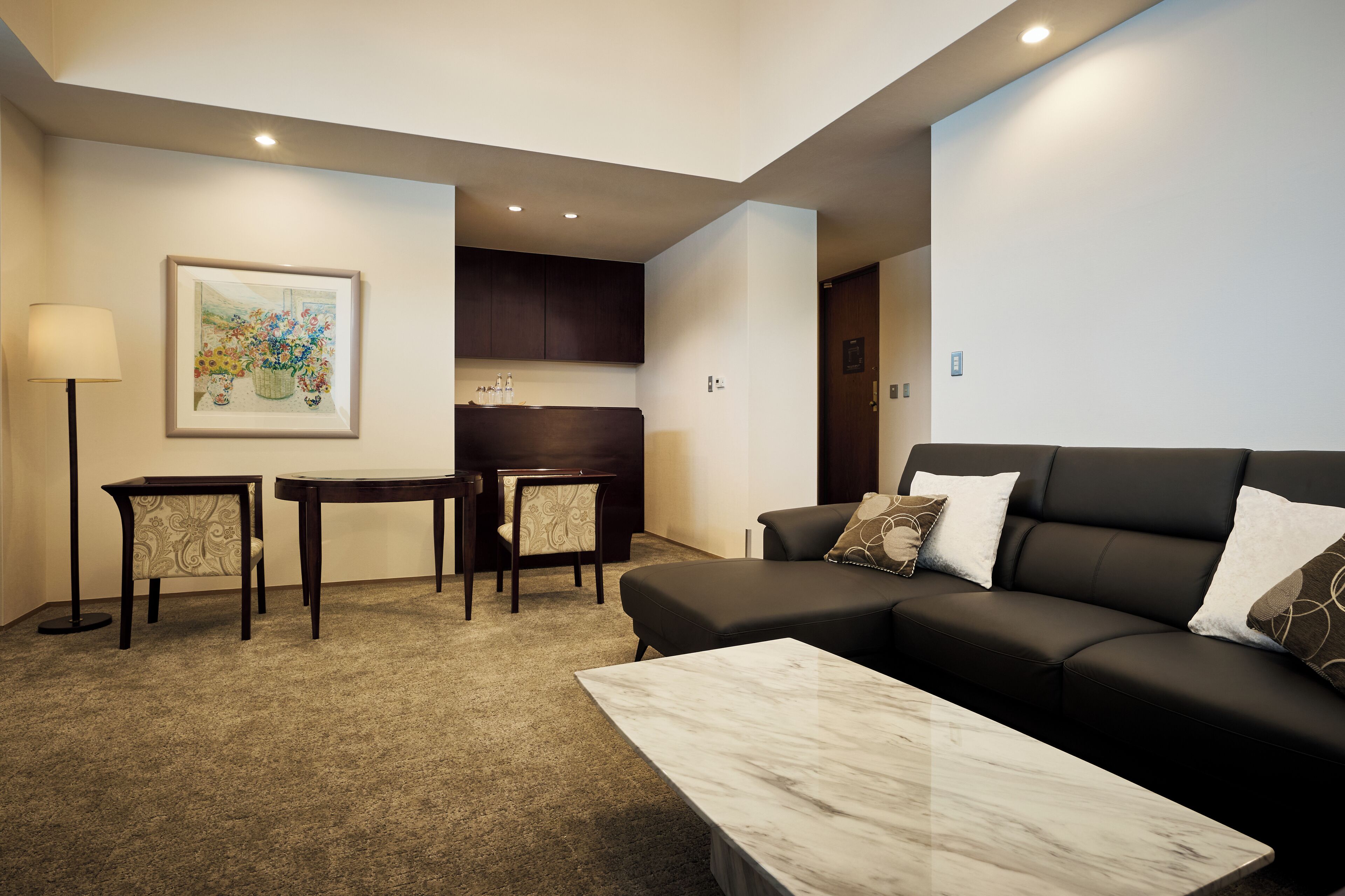 A modern living room with a black leather sofa, a marble coffee table, and a dining area with a small table and chairs.