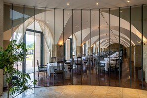 A spacious restaurant with high ceilings and large windows, offering a view of the outdoors.