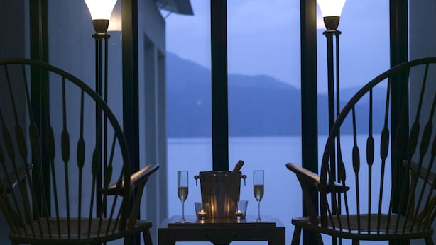 Una mesa con una botella y vasos, dos sillas y vistas a un cuerpo de agua.