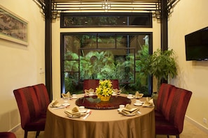 A dining area with a round table, red upholstered chairs, and a large window with a view of greenery.