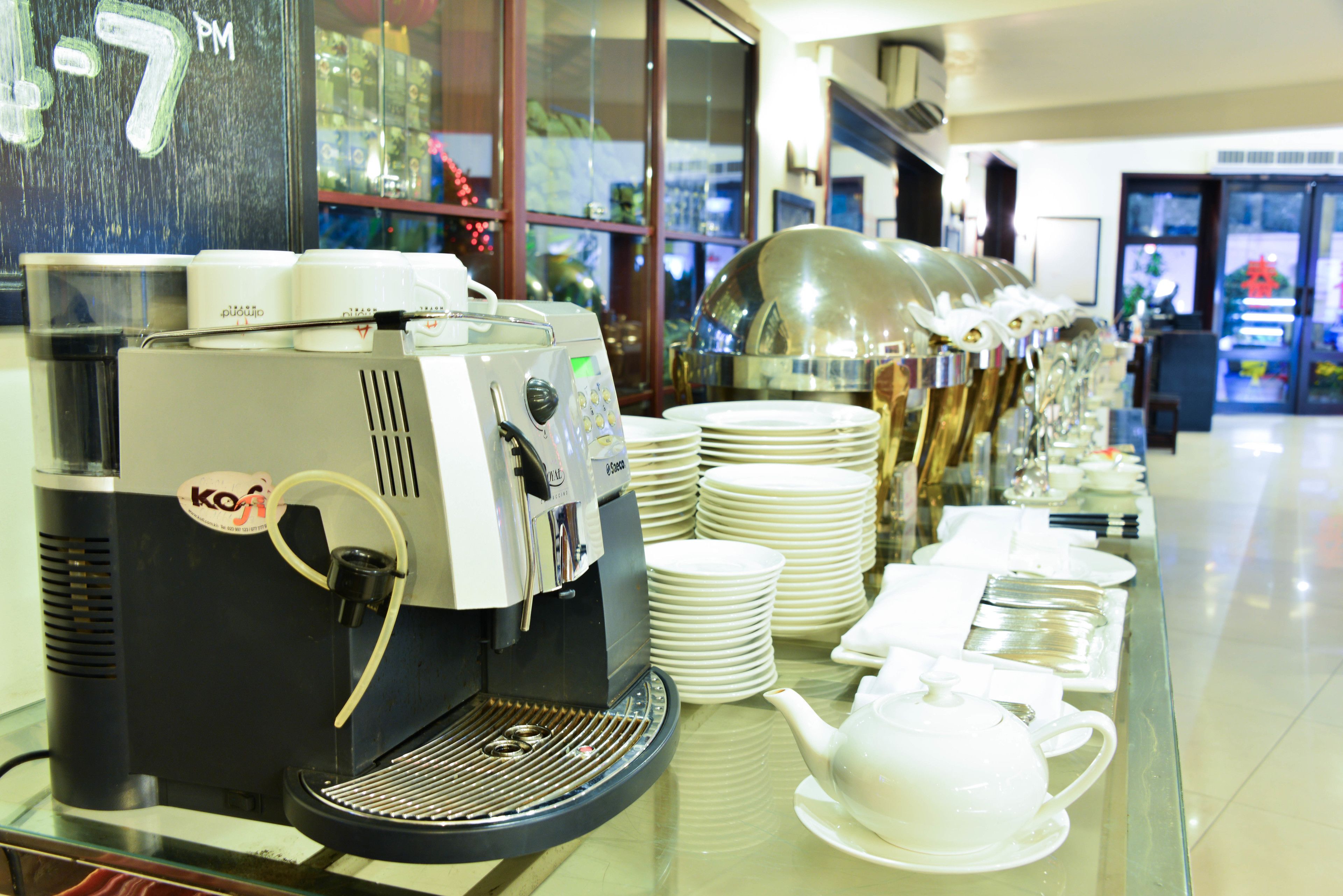 A coffee station with a coffee machine, stacks of white plates, and a teapot on a glass counter.