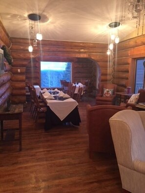 Interior de una cabaña de troncos con comedor, una mesa dispuesta para cuatro personas rodeada de sillas de madera.