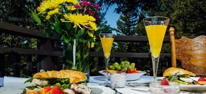 Una mesa al aire libre con diversas opciones de comida, como sándwiches, frutas y un vaso de jugo de naranja.