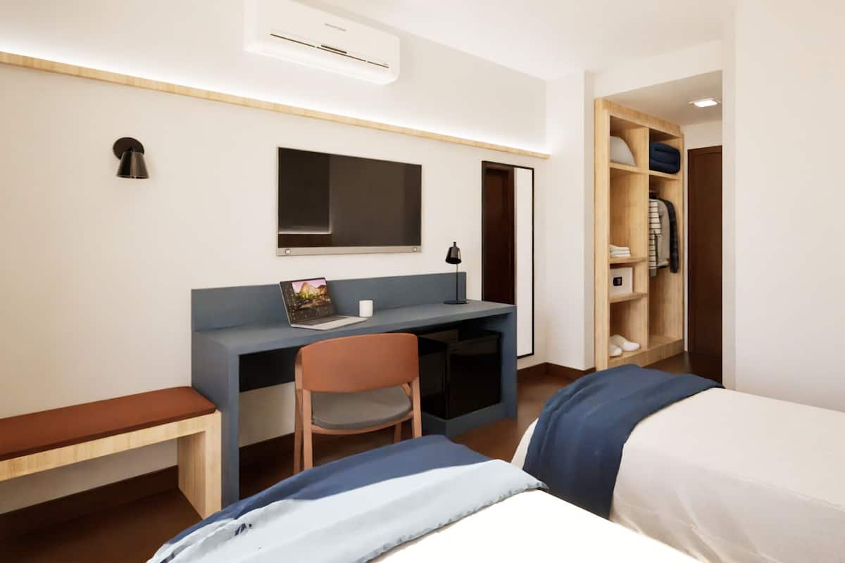 A compact hotel room with a single bed, a desk with a laptop, a chair, a small table, and a wardrobe.