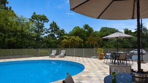 A swimming pool with tiled flooring, surrounded by a fence, and outdoor seating with umbrellas. - Matiz Barão Geraldo Express (Campinas)