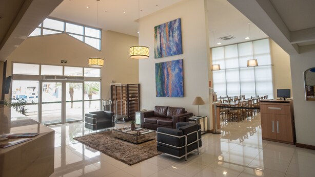 A spacious lobby with a high ceiling, a seating area with a brown leather sofa and armchairs, a coffee table, and a dining area with a large table and chairs. - Matiz Barão Geraldo Express (Campinas)