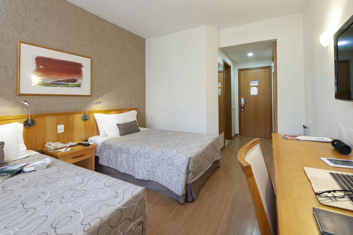 A hotel room with two beds, a desk with a laptop, a telephone, and a television.