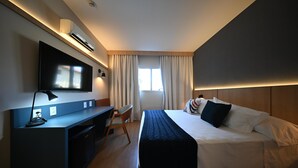 A modern hotel room with a flat-screen TV, a desk with a chair, a bed with pillows, and a window with curtains. - Matiz Barão Geraldo Express (Campinas)