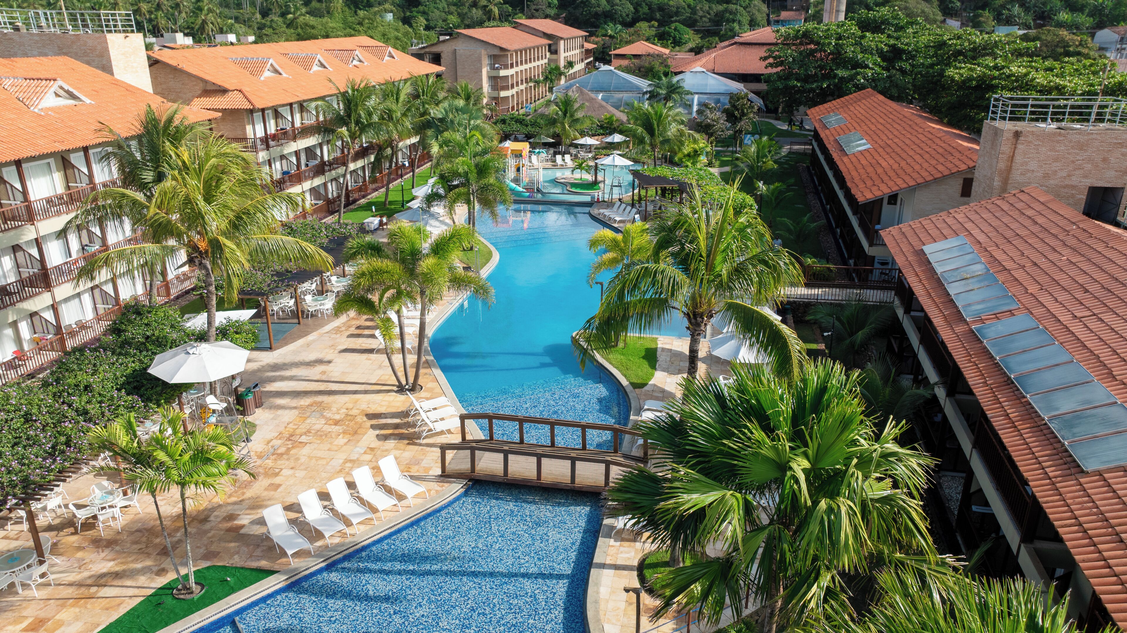 Un resort con piscina central, palmeras y un puente que conecta diferentes zonas.