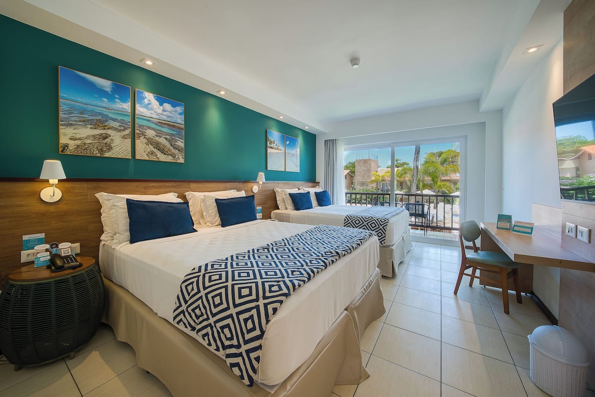 A hotel room with two beds, a desk, and a balcony with a view.
