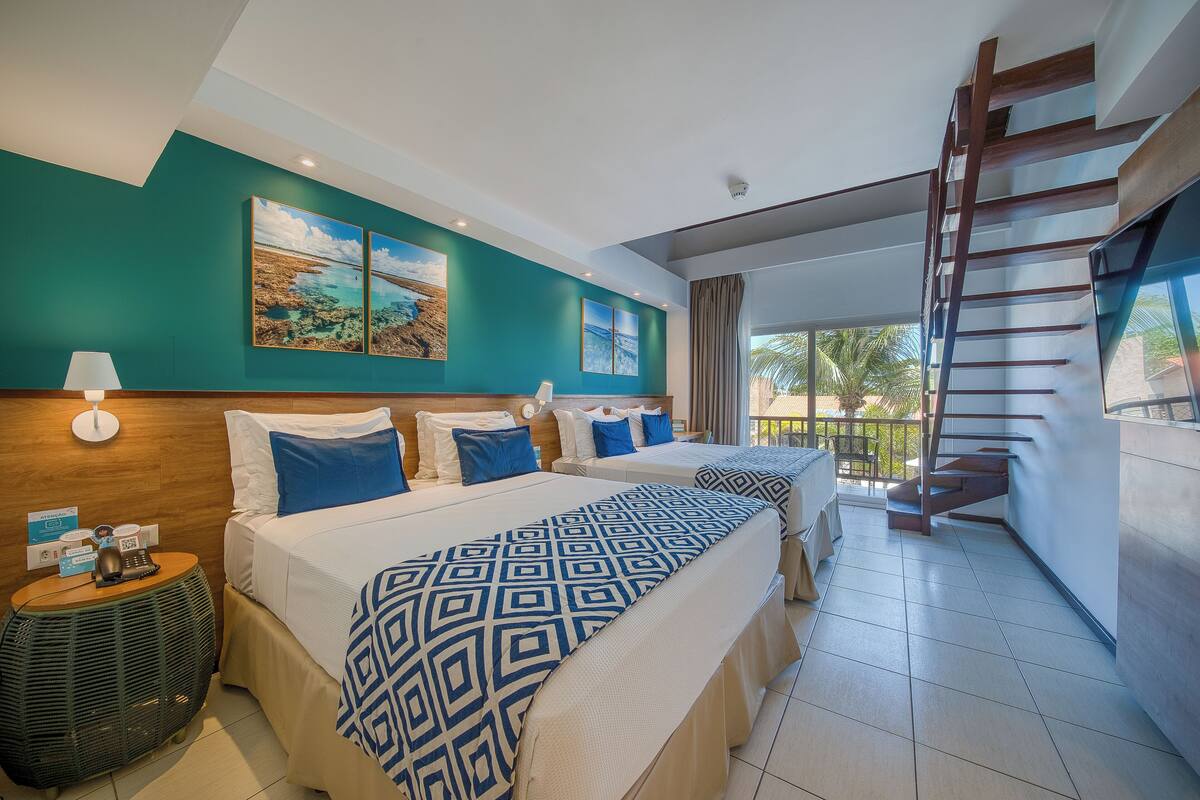 A hotel room with two beds, a wooden headboard, a large window, and a staircase.
