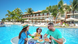 A poolside dining area with a table, chairs, and a view of the pool and hotel building. - Salinas Maceió All Inclusive Resort (Maceió)